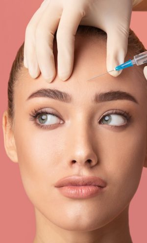 Skin Lifting Injection. Young Woman Receiving Botox Beauty Injection In Forehead Standing Over Pink Background. Studio Shot